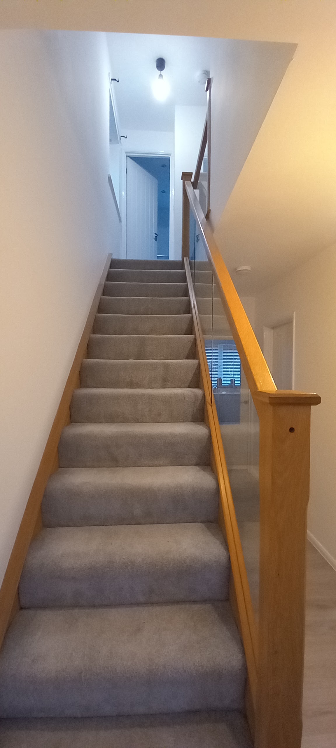 A staircase with an oak and glass balustrade and freshly painted walls